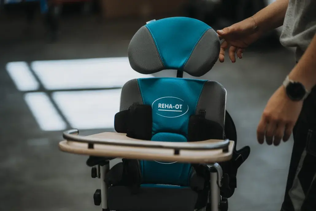 Eine Person justiert einen Rehatechnik-Stuhl mit REHA-OT-Logo in einer Werkstatt.