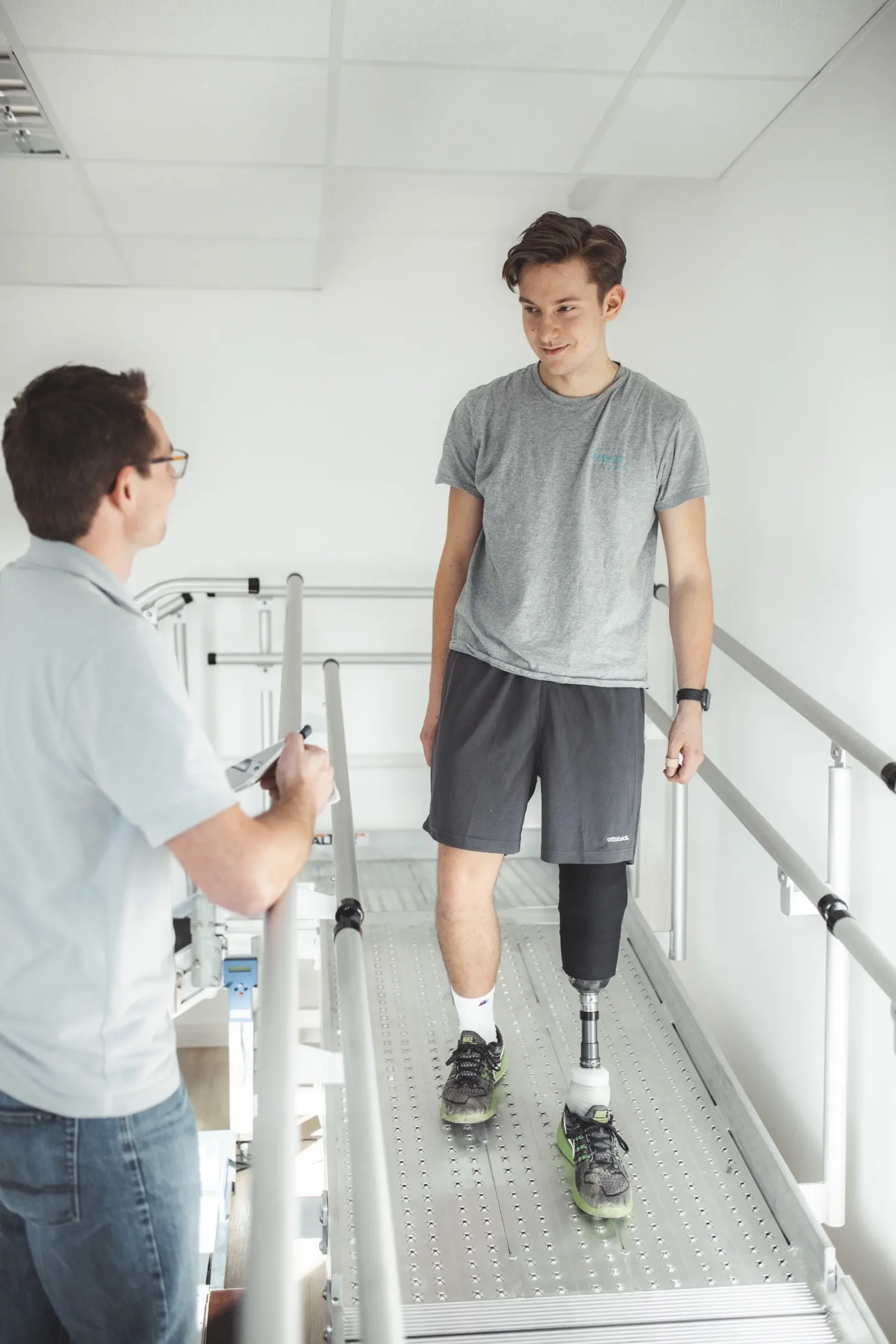 Ein Mann mit Beinprothese übt das Gehen auf einer Gehstrecke mit einem Orthopädietechniker.