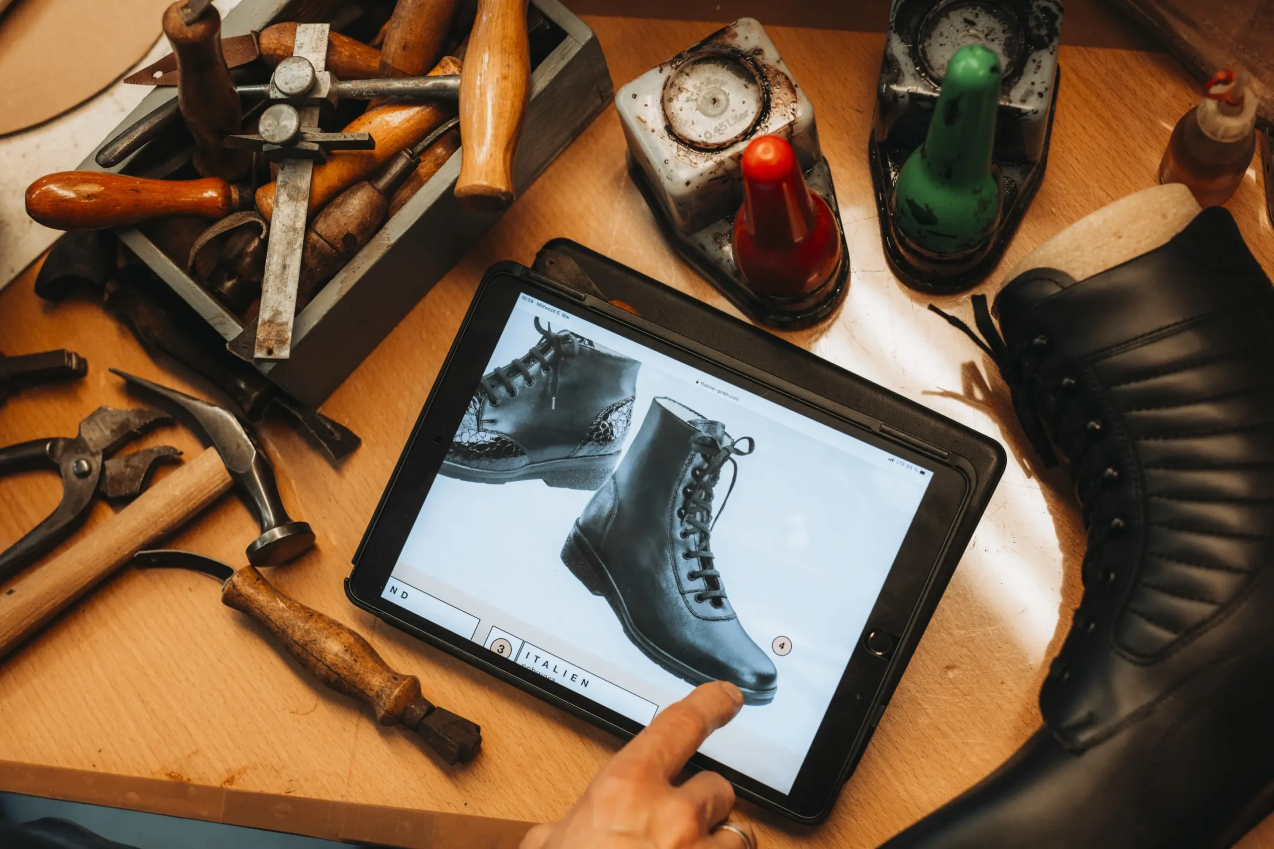 Ein Tablet zeigt orthopädische Schuhe in einer Werkstatt mit Werkzeugen.