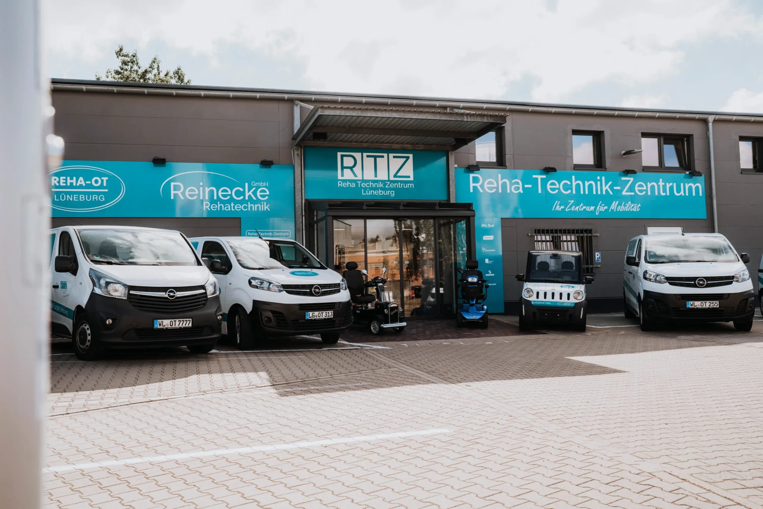 Reha-Technik-Zentrum mit mehreren Fahrzeugen und Elektromobilen vor dem Gebäude. Sanitätshaus, Rehatechnik.
