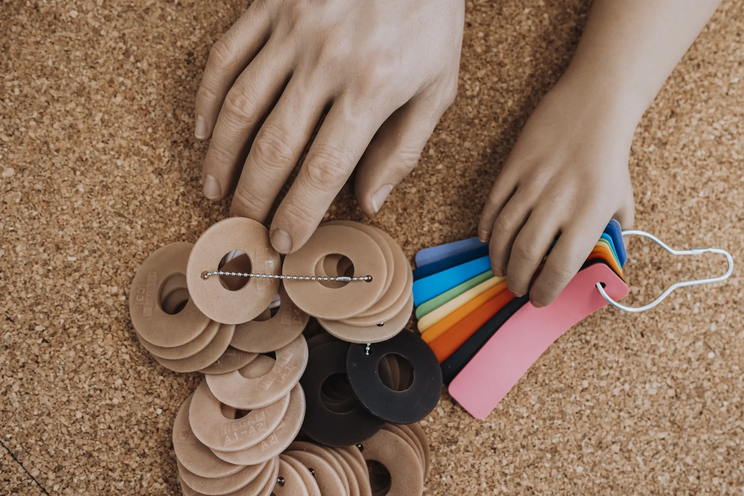 Hände halten Materialproben in verschiedenen Farben auf einer Korkoberfläche. Kontext: Orthopädietechnik.