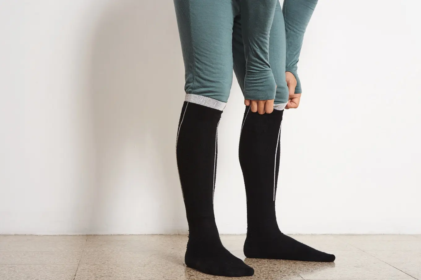 Eine Person zieht schwarze Kompressionsstrümpfe über grüne Leggings an.
