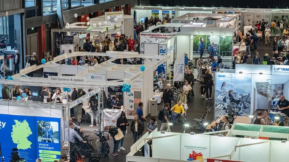 Große Messehalle mit zahlreichen Messeständen und vielen Besuchern, darunter auch Menschen im Rollstuhl. Stände präsentieren verschiedene Produkte und Dienstleistungen, teilweise mit Rollstuhl- und Mobilitätshilfen. Atmosphäre wirkt lebhaft und gut besucht.